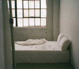 Empty bed with white sheets in a concrete room