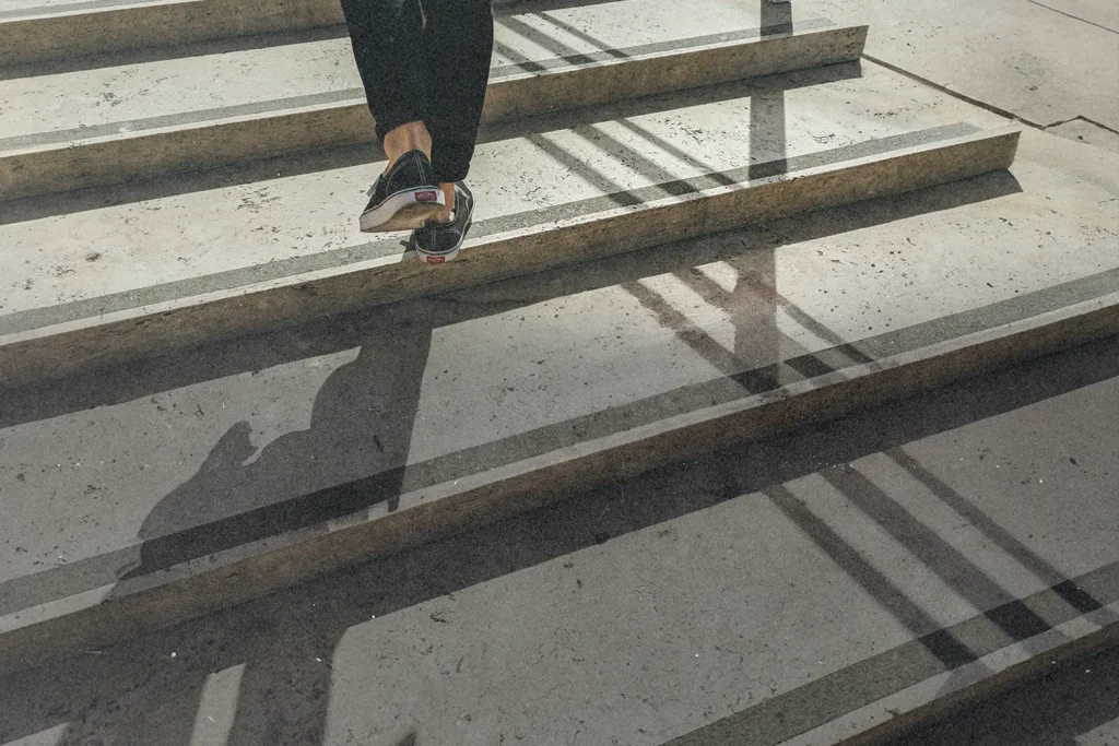 Person walking up concrete steps with sunlight casting long shadows across the staircase