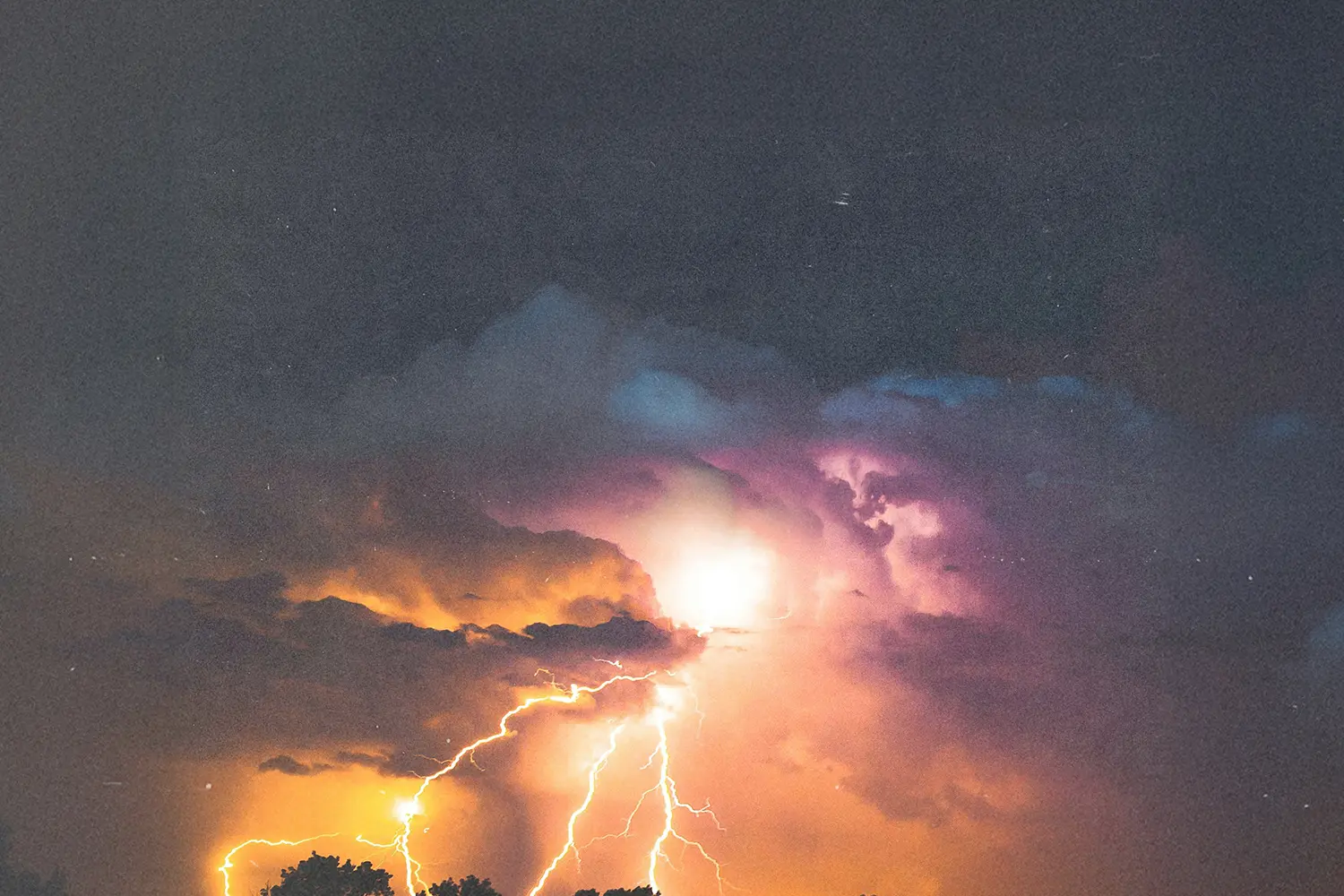 Bright lightning bolts illuminating dark storm clouds with vivid orange and purple tones