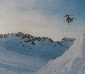 Person performing a midair ski jump above a snowy slope with rugged mountains in the background