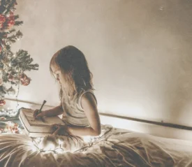 A little girls journaling by the Christmas tree, thinking of her Christmas wish for the season
