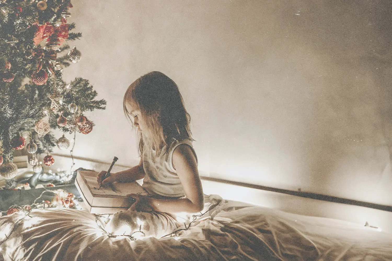A little girls journaling by the Christmas tree, thinking of her Christmas wish for the season