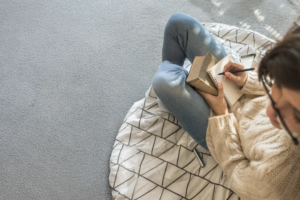 Woman writing in a notebook at a cozy desk, practicing gratitude journaling in a peaceful, softly lit room.