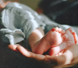 Close-up of newborn feet resting in a caring hand, reflecting God’s Gift of life, the true Christmas gift, and the hope found in God’s Plan for us all.
