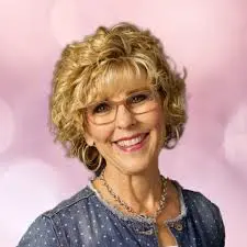 A woman smiling in a portrait-style image against a soft pink background.