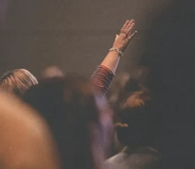 A woman in church raising her hands in worship, believing just like you that God Loves You