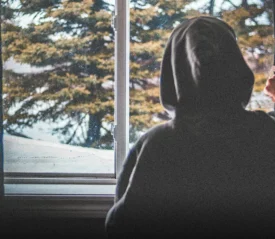 A person in a hoodie looks out a window on a cold day, reflecting on doubt and hope, symbolizing someone you love who may be questioning God in a hard season.