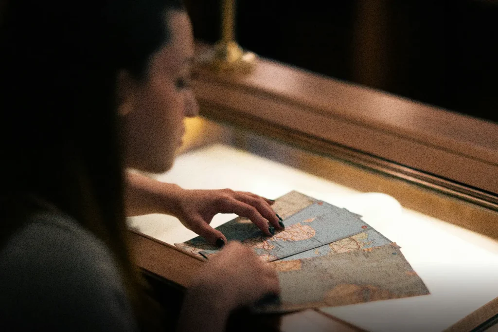 Hands examining an aged map inside a lit display case.
