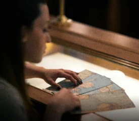 Hands examining an aged map inside a lit display case.
