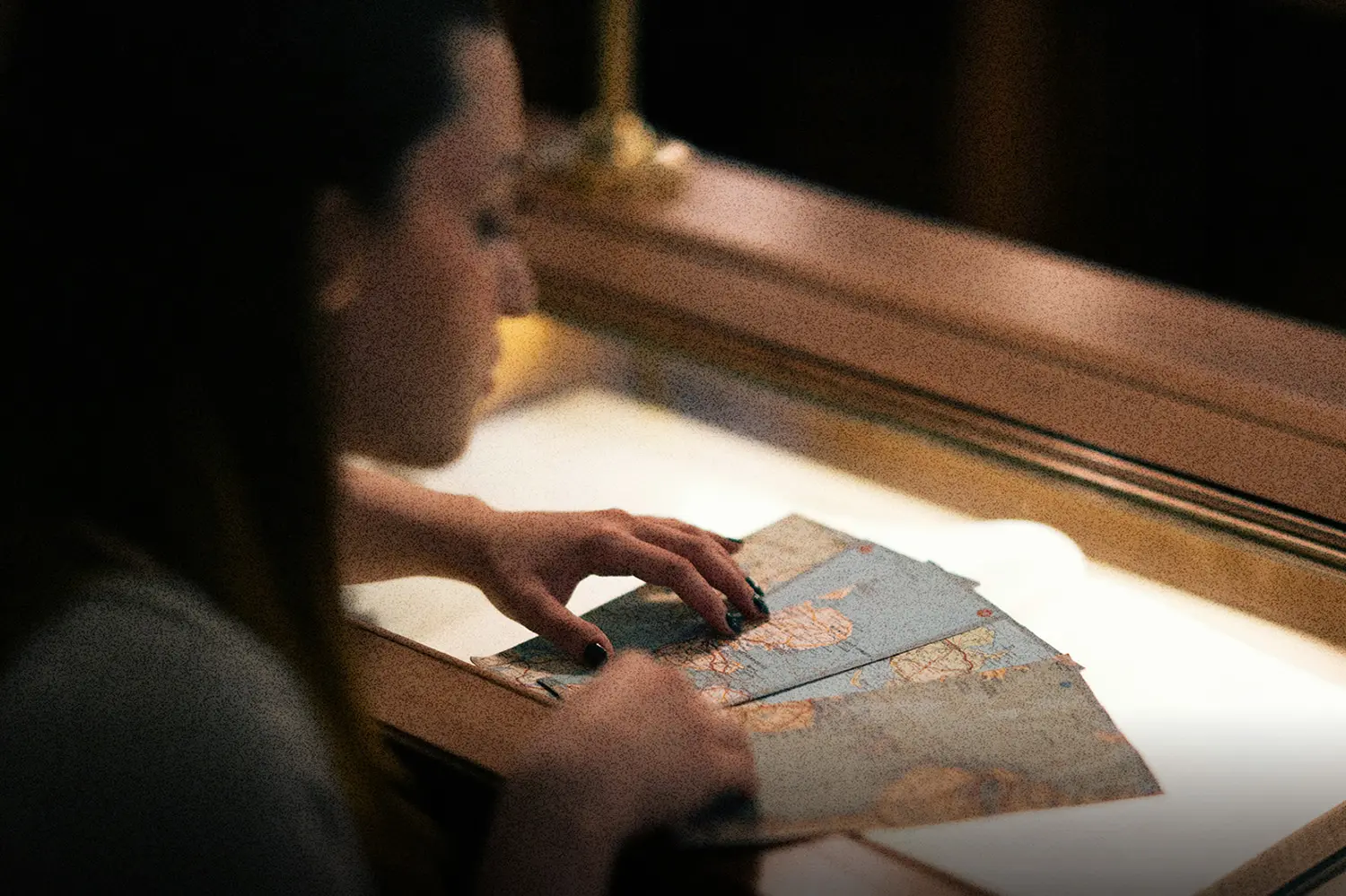 Hands examining an aged map inside a lit display case.