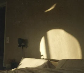 Sunlight casting soft shadows on a bedroom wall above an unmade bed.