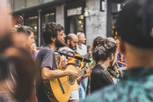 A street musician playing guitar during an outdoor performance, surrounded by people in a city area.