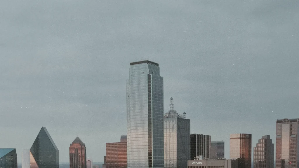 A wide view of the Dallas, Texas skyline featuring tall buildings and skyscrapers under a cloudy sky.