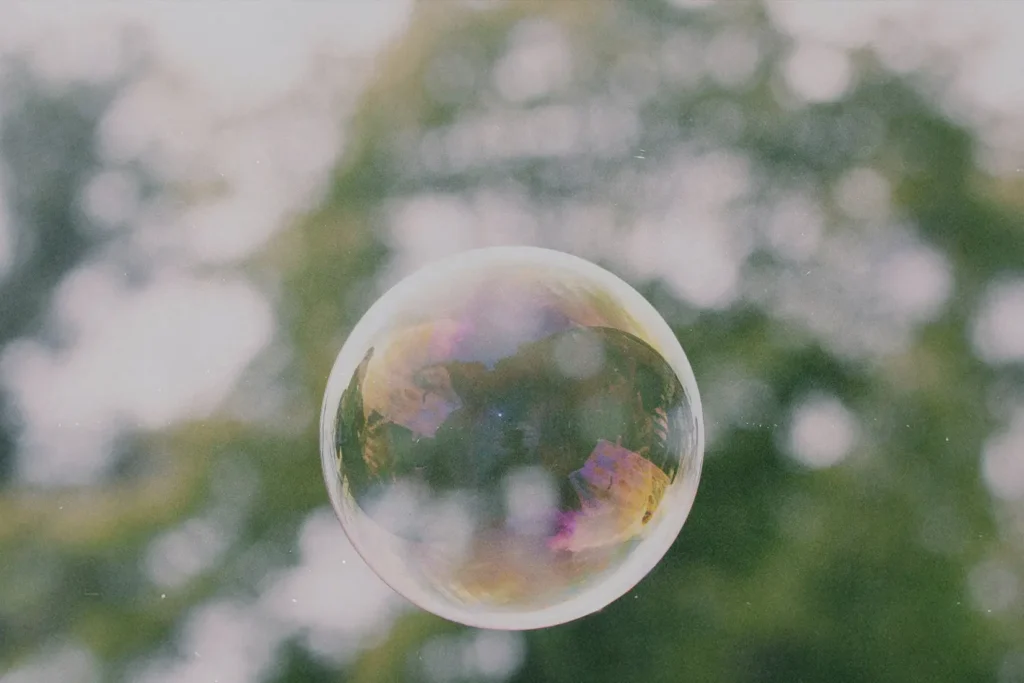 A translucent soap bubble floating outdoors against a softly blurred green background.