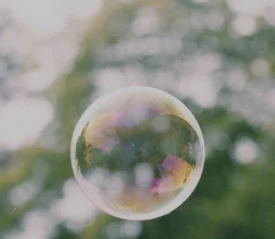 A translucent soap bubble floating outdoors against a softly blurred green background.